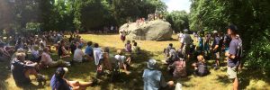 Large group of people surrounding a boulder. 