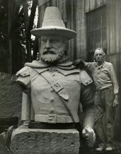 Large bust sculpture of Pilgrim Myles Standish with man standing next to it.
