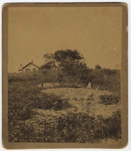 Image of field with bare spot, house in background. Site of Myles Standish's grave, Duxbury.